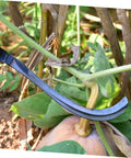 Close-up of a Two Piece Multi Function Mowing Tool Rustproof Scythe for weeding, cutting a plant stem in a garden.