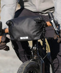 Cyclist using Dayliner Mini Roll Top Handlebar Bag 3 L Waterproof Commuter Sling With Shoulder Strap And Reflective Detail Recycled Ripstop Ideal For City Ride MTB Trek Work Or Weekend Getaways on front of bike