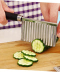 Stainless steel wavy chopper with ergonomic black handle slicing cucumber on a wooden cutting board