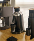Top Shelf Single Dose Coffee Grinder Equipped With 83Mm Red Titanium Flat Burrs And Integrated Plasma Ionizer Chute For Zero Static Clumps Ideal For Home Brew Crews Chasing Consistent Pulls Without Any Headache In Classic Black on a kitchen countertop with espresso machine.