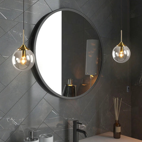 Mid Century Modern Brushed Gold Pendant Light with Plug In Cord, Smoke Gray Glass Globe hanging beside a round mirror in a bathroom