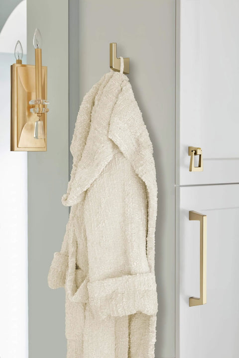 Golden Champagne Blackrock Cabinet Pull Drawer Pull And Drawer Handle For Cabinets And Drawers In Transitional Style Six And Five Sixteenth Inch Center To Center Seven And Quarter Inch Overall Length One Pack Cabinet Hardware Amerock installed on white cabinet next to robe hook.