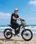Man riding All-Terrain Electric Dirt Bike For Adults With 1536Wh Battery And 32Ah, on sandy beach, 25 inch fat tires visible.