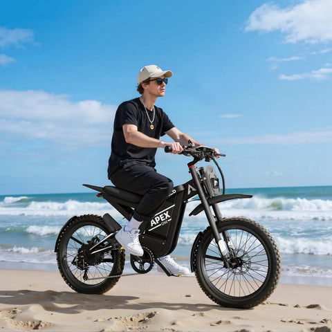 Man riding All-Terrain Electric Dirt Bike For Adults With 1536Wh Battery And 32Ah, on sandy beach, 25 inch fat tires visible.