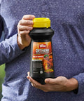 Person holding a bottle of Ortho Fire Ant Killer, 12 oz, with yellow cap, outdoor setting, focus keyword: Fire Ant Killer For Outdoors No Watering Needed Kills Queens Mound Treatment Treats Up To 162 Mounds 12 Oz Per Bottle 2 Pack Easy Two Step System For Fast Outdoor Ant Control Long Lasting Results For Easy All Day Control.
