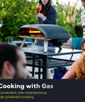 Koda 16 Natural Gas Pizza Oven for Outdoor Cooking 16 inch gas powered pizza oven with regulator and hose in use on patio table.