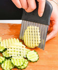 Front view of a stainless steel crinkle cutter with black handle slicing ridged cucumber slices on a wooden board