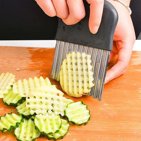 Front view of a stainless steel crinkle cutter with black handle slicing ridged cucumber slices on a wooden board