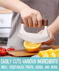Rocking mezzaluna knife with walnut wood handle and stainless steel curved blade slicing an orange on a cutting board.