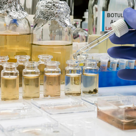 Lab scene with hand using pipette over sterile glass vials for injection and peptide storage, with various fluids for research.