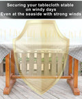 Outdoor table with shield illustration showing Hidden Strap Tablecloth Clips For Windy Picnics And Thick Indoor Outdoor Tables Invisible Design Keeps Your Tablecloth Secure Without Visible Clips On Any Surface.