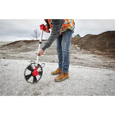 User operating Built Like A Tank 12 Inch Digital Measuring Wheel on gravel ground for accurate measurements outdoors.