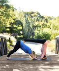Two people practicing yoga on an XL Rubber Yoga Mat 78 Inch By 28 Inch Storm Color With Dual Sided Non Slip Grip on a wooden bridge.