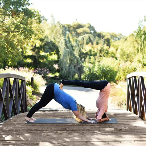 Two people practicing yoga on an XL Rubber Yoga Mat 78 Inch By 28 Inch Storm Color With Dual Sided Non Slip Grip on a wooden bridge.