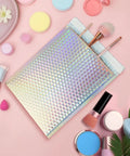 25 Pack Holographic Bubble Mailers 9 By 12 Self Seal Waterproof Poly Padded Envelopes next to cosmetics and brushes on pink background