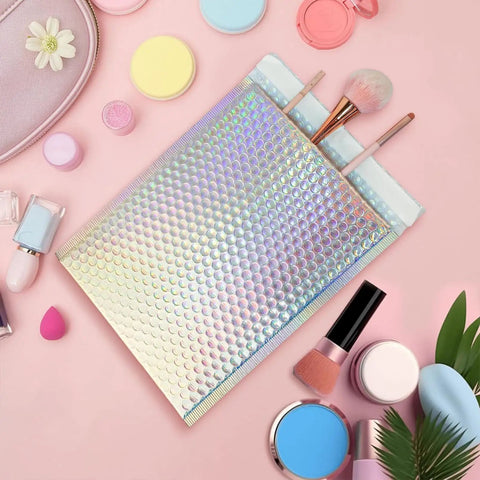 25 Pack Holographic Bubble Mailers 9 By 12 Self Seal Waterproof Poly Padded Envelopes next to cosmetics and brushes on pink background