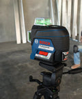 Close-up of Boss Class 12V Max Three Plane Green Beam Laser Level on tripod in construction setting with contractor.