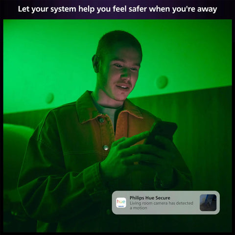 A person using a smartphone with a smart home security app interface, green ambient lighting in the room.