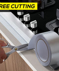 Silver aluminum foil heat shield tape roll, 2in x 66ft, being cut with scissors beside a gas stove