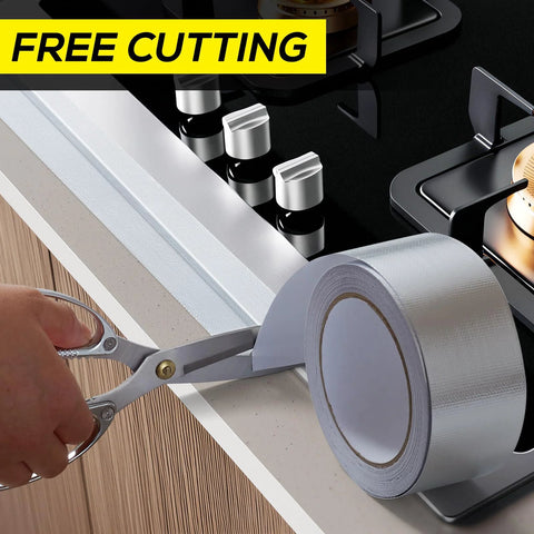 Silver aluminum foil heat shield tape roll, 2in x 66ft, being cut with scissors beside a gas stove