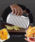 Stainless steel crinkle cutter with black handle slicing potatoes into crinkle-cut fries (front view).