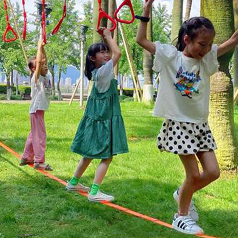 Children balancing on 65ft Ninja Slackline Kit With Ratchet System And Tree Protectors, 500lb Capacity Backyard Set.