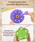 Hands assembling 3D Dahlia Flower Wooden Puzzle Kit For Adults on a table showing flower and green base with adhesive tape.