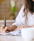 Person writing in a notebook with Super Smooth Hybrid Ink Ballpoint Pens with Black 0.7 Mm Fine Point Tips Pack of 3.