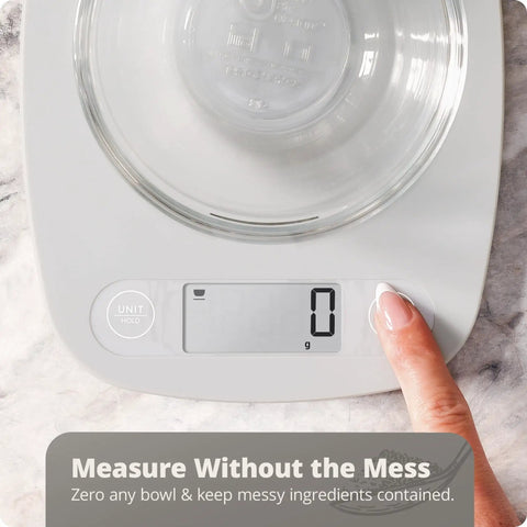 Go-To Slim Digital Kitchen Scale With 1g Precision showing tare function with finger pressing button, glass bowl on top