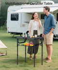 Foldable Camping Table With Storage Net 23.2 x 16 inches, adjustable height, set up outdoors with a caravan in the background.