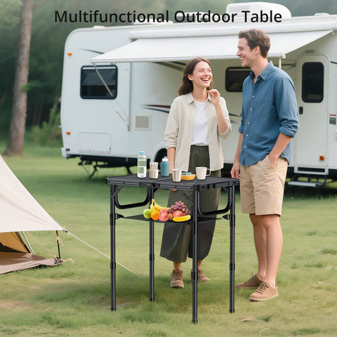 Foldable Camping Table With Storage Net 23.2 x 16 inches, adjustable height, set up outdoors with a caravan in the background.
