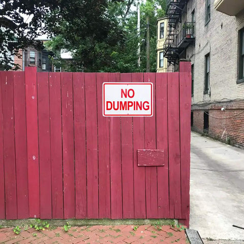 Heavy Duty Aluminum No Dumping Signs Two Pack on a red wooden fence in an urban area, preventing illegal dumping.