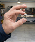 Hand holding 30Pcs 304 Stainless Steel Hose Clamps Set With 6-51mm Adjustable Worm Gear Clamps in a workshop.