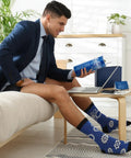 Man wearing gear-patterned socks from Six Piece Engineering Graduation Gift Set For Men Including Stainless Tumbler Cup, Engineering Ruler, Engineer Socks, Keychain, Greeting Card, And Gift Box Great For Mechanical Engineering Students, Retirement Or Graduation Day reading a book in a home office setting