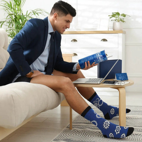 Man wearing gear-patterned socks from Six Piece Engineering Graduation Gift Set For Men Including Stainless Tumbler Cup, Engineering Ruler, Engineer Socks, Keychain, Greeting Card, And Gift Box Great For Mechanical Engineering Students, Retirement Or Graduation Day reading a book in a home office setting