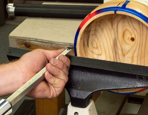 Woodturning tool, 12-inch stainless steel, 90° carbide, unhandled, held by hand at a wood lathe with a round wooden blank.