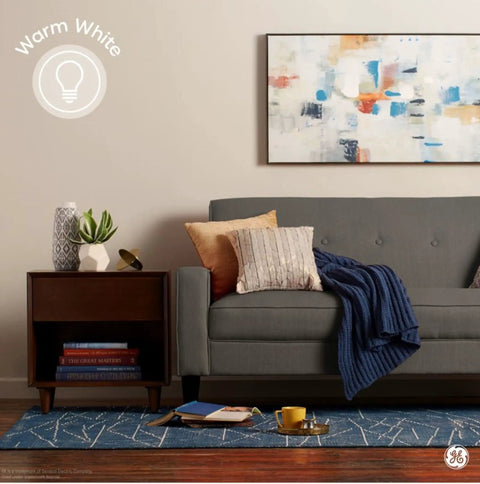 Living room with blue rug, gray sofa, art on wall, and text 'Warm White' illustrating Vintage Style LED Light Bulbs 6W 60W Equivalent Amber Glass.