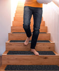 Person walking down stairs with 15 Piece Indoor Stair Treads For Wooden Steps Grippy Non Slip Carpet Treads With Gray Stripe Design Polyester Runner Mats