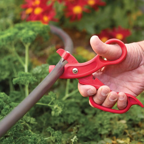 Premium Drip Irrigation Tubing Cutter And Hole Punch Tool Kit Two Pack With Comfy Grip cutting a poly tube in a garden.
