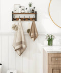 Rustic Wood Wall Shelf With Five Metal Hooks Coat Rack For Your Entryway Hallway Bathroom Mudroom And Bedroom Keeps Hats Coats Purses Towels Sorted And Chic In Rustic Brown And Black Finish mounted on a white bathroom wall with towels hanging.