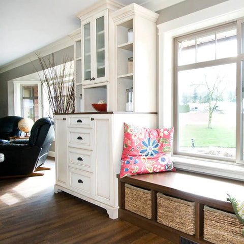 Bright living room with cabinets, a colorful pillow on a bench, and large windows offering a scenic view.