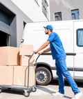 Person in blue uniform pushing a cart with boxes near a delivery van outside a warehouse