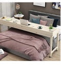 Spacious Wooden Overbed Computer Desk With Smooth Rolling Casters And Secure Safety Baffle Slick Laptop Station For Bedside Chill Or Remote Working Easy Room Mobility on a bed with laptop and plants.