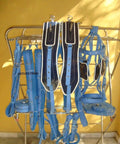 Two Tone Synthetic Patent Leather Driving Harness For Double Horse Cart With Extra Padding Double Layer Nose Band And Hand Carved Saddle And Bridle In Blue And Black displayed on a rack.