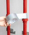 Applying Heavy Duty Duct Tape 1.88 Inch Wide By 45 Yard Silver, 12 Pack For Repairs, Patching, Packaging, Bundling And General Quick Fixes With Strong Adhesive That Sticks To Most Surfaces around red pipes.