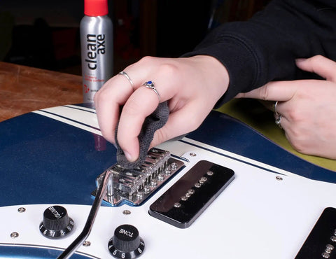 Person cleaning a guitar bridge with a microfiber cloth, using Complete Guitar Care Kit And Clean Polish Set With Fretboard Conditioner.
