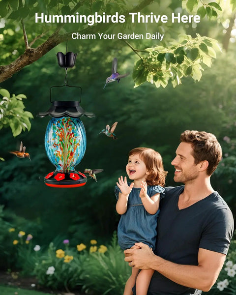 Man and child admiring Solar Powered Hummingbird Feeder With 49 Fl Oz Capacity Hand Blown Blue Glass Color Changing Night Glow Seven Feeding Ports With Perch Never Leaks Outdoor Hanging For Your Yard in a garden setting.