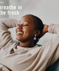 Person relaxing on couch, text 'breathe in the fresh', promoting Plug In Air Freshener Starter Kit With Odor Fighting Scented Oils.