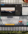 Ultra Slim Wireless Mechanical Keyboard With 100 Keys And Custom RGB Backlit Lighting Featuring Bluetooth Five Point One And Fast Wired Modes For Pcs Mac Laptops In Sleek Grey With Smooth Gateron Aloe Switches That Hit Different Daily on a table next to a tablet and phone.