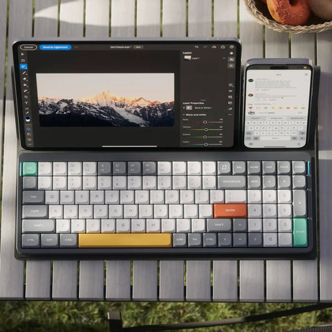 Ultra Slim Wireless Mechanical Keyboard With 100 Keys And Custom RGB Backlit Lighting Featuring Bluetooth Five Point One And Fast Wired Modes For Pcs Mac Laptops In Sleek Grey With Smooth Gateron Aloe Switches That Hit Different Daily on a table next to a tablet and phone.
